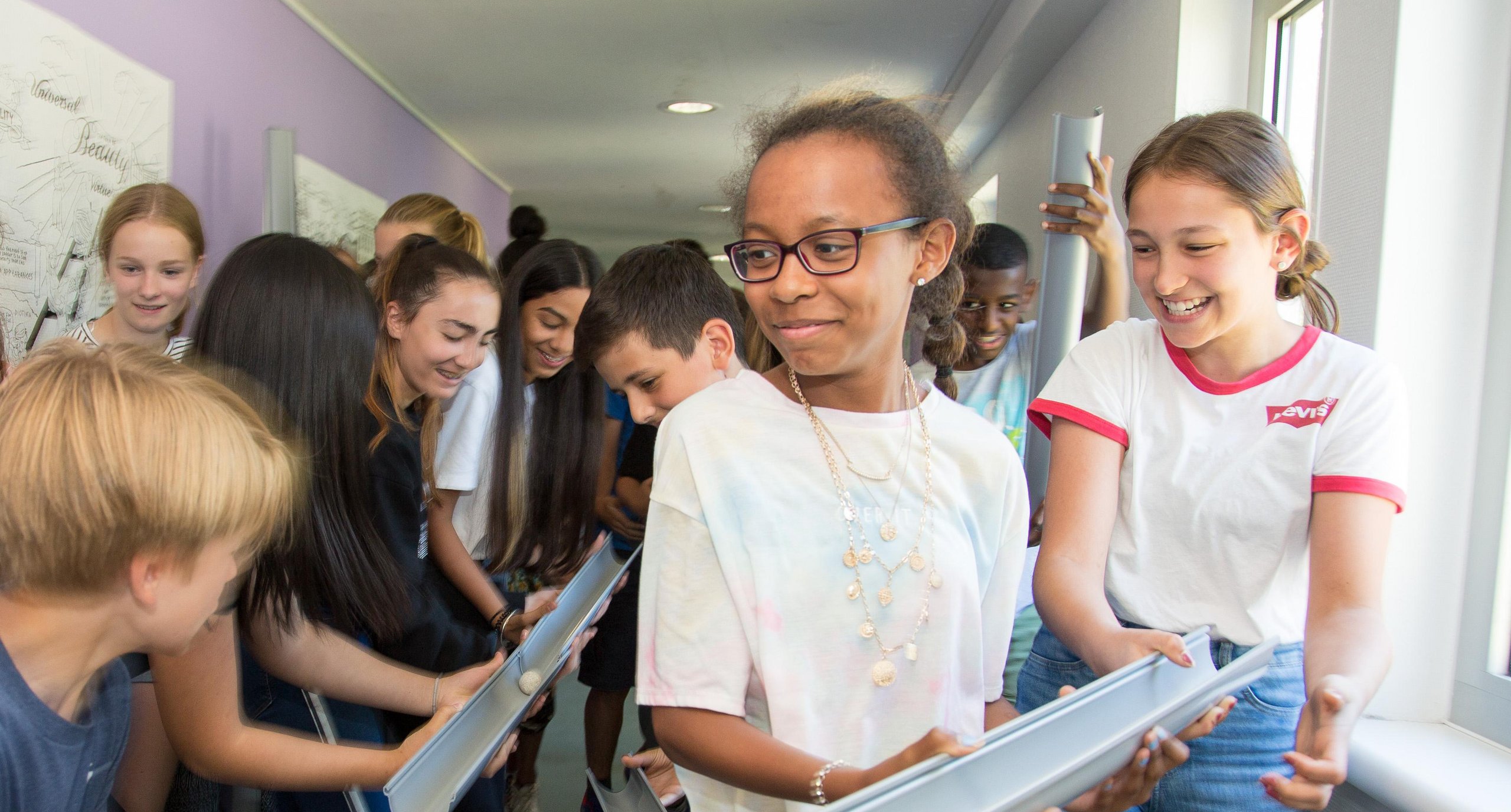 Eine Gruppe verschiedener Schüler lächelt und arbeitet zusammen, um einen Ball durch verbundene Rohre in einer Schule zu führen.
