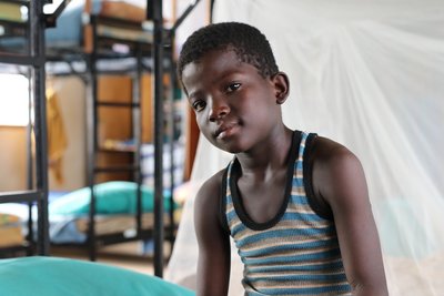 Porträt eines jungen schwarzen Jungen in gestreiftem Unterhemd, der in die Kamera blickt, mit unscharfem Innenhintergrund.
