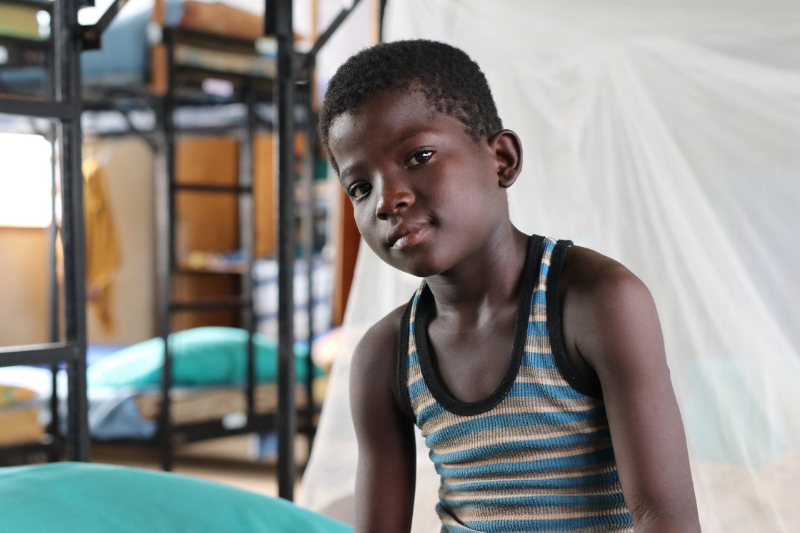 Porträt eines jungen schwarzen Jungen in gestreiftem Unterhemd, der in die Kamera blickt, mit unscharfem Innenhintergrund.