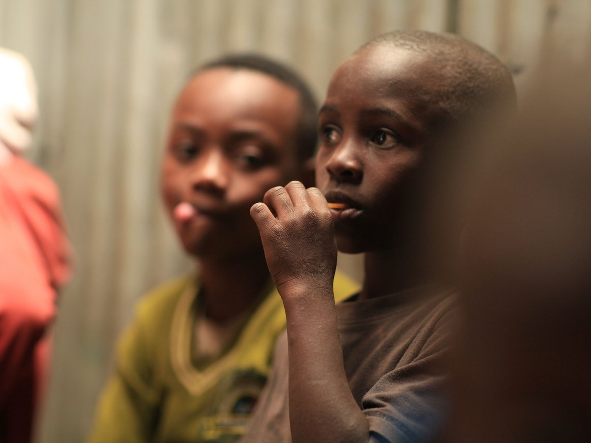 Nahaufnahme eines jungen Kindes, das etwas zum Mund hält, ein anderes Kind unscharf im Hintergrund.