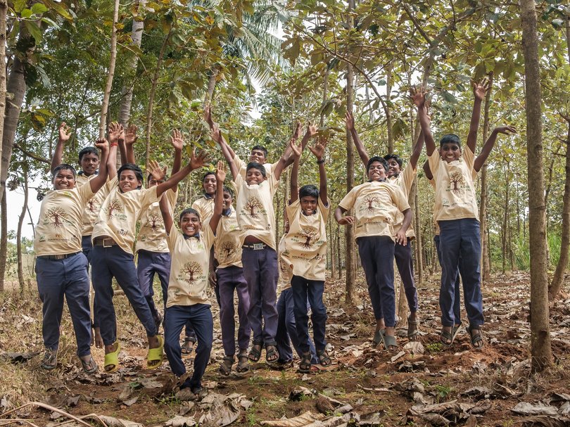 Eine Gruppe lachender Jungen springt in einem Wald und trägt T-Shirts mit dem Logo „WE WANT A GREEN WORLD“.