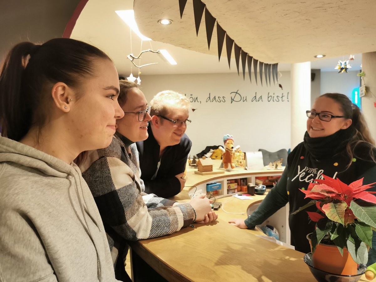 Drei Gäste unterhalten sich an einem Tresen mit einer lächelnden Frau, umgeben von festlicher Dekoration und einem Weihnachtsstern.