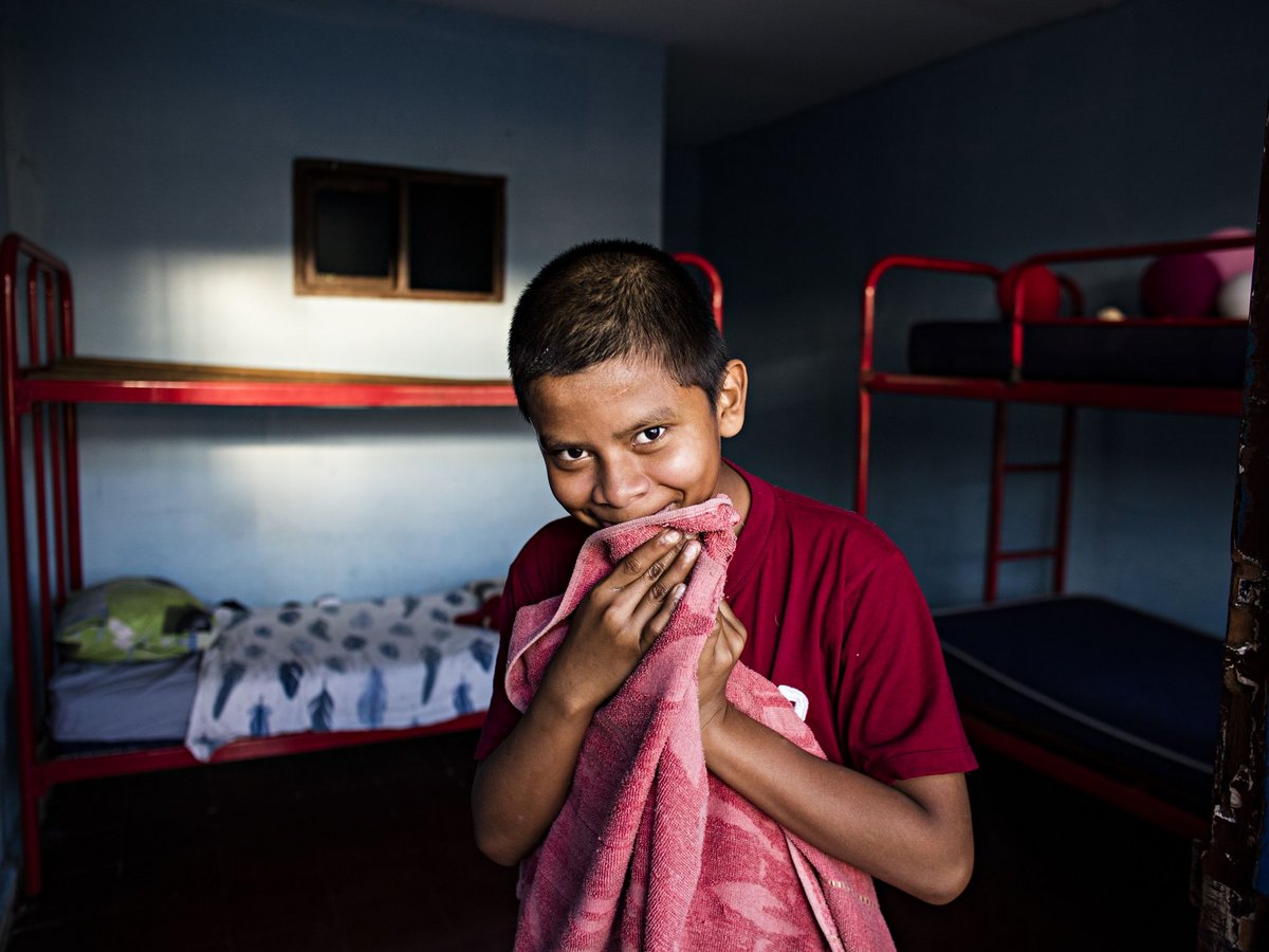 Lächelnder Junge in rotem Shirt hält rosafarbenes Handtuch vor sein Gesicht, rote Etagenbetten in blauem Zimmer.