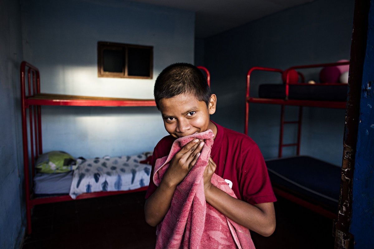 Lächelnder Junge in rotem Shirt hält rosafarbenes Handtuch vor sein Gesicht, rote Etagenbetten in blauem Zimmer.