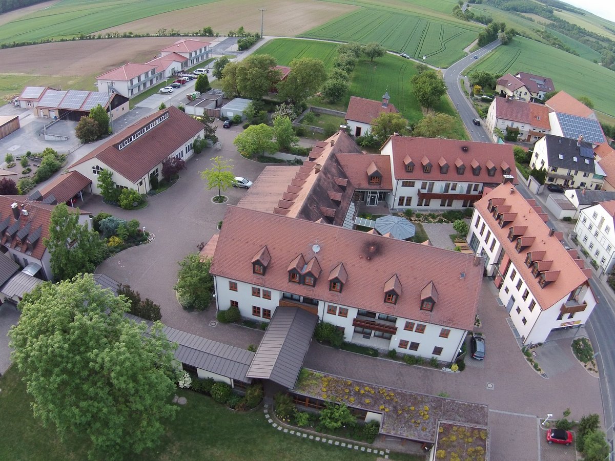 Vogelperspektive auf eine ländliche Siedlung mit vielen roten Dächern, Solaranlagen, Feldern und kurvigen Straßen.