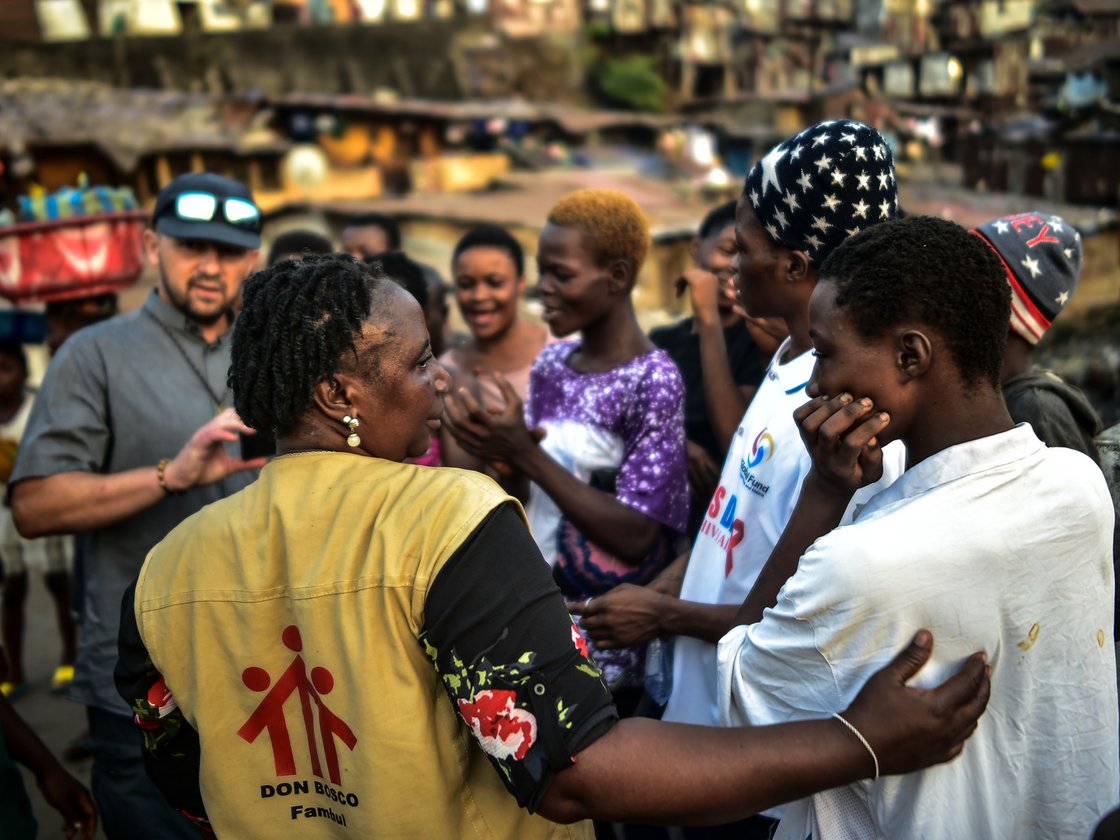 Don Bosco Helferin im Gespräch mit jungen Menschen in einer lebhaften, dicht besiedelten Gemeinde.