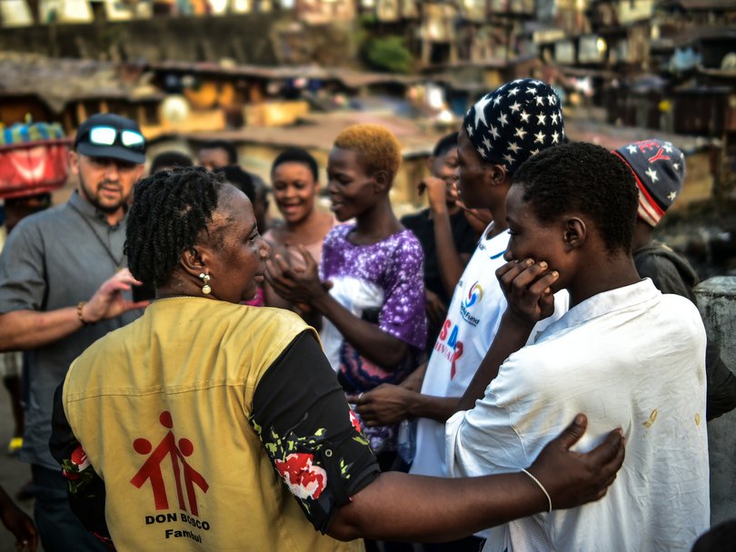 Don Bosco Helferin im Gespräch mit jungen Menschen in einer lebhaften, dicht besiedelten Gemeinde.