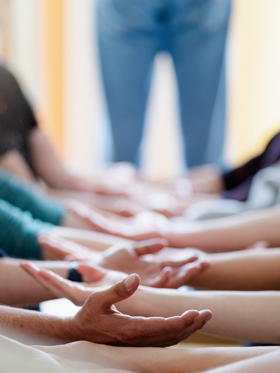 Mehrere Hände mit offenen Handflächen bilden einen Kreis, der Einheit, Gemeinschaft oder eine gemeinsame Praxis vermittelt.