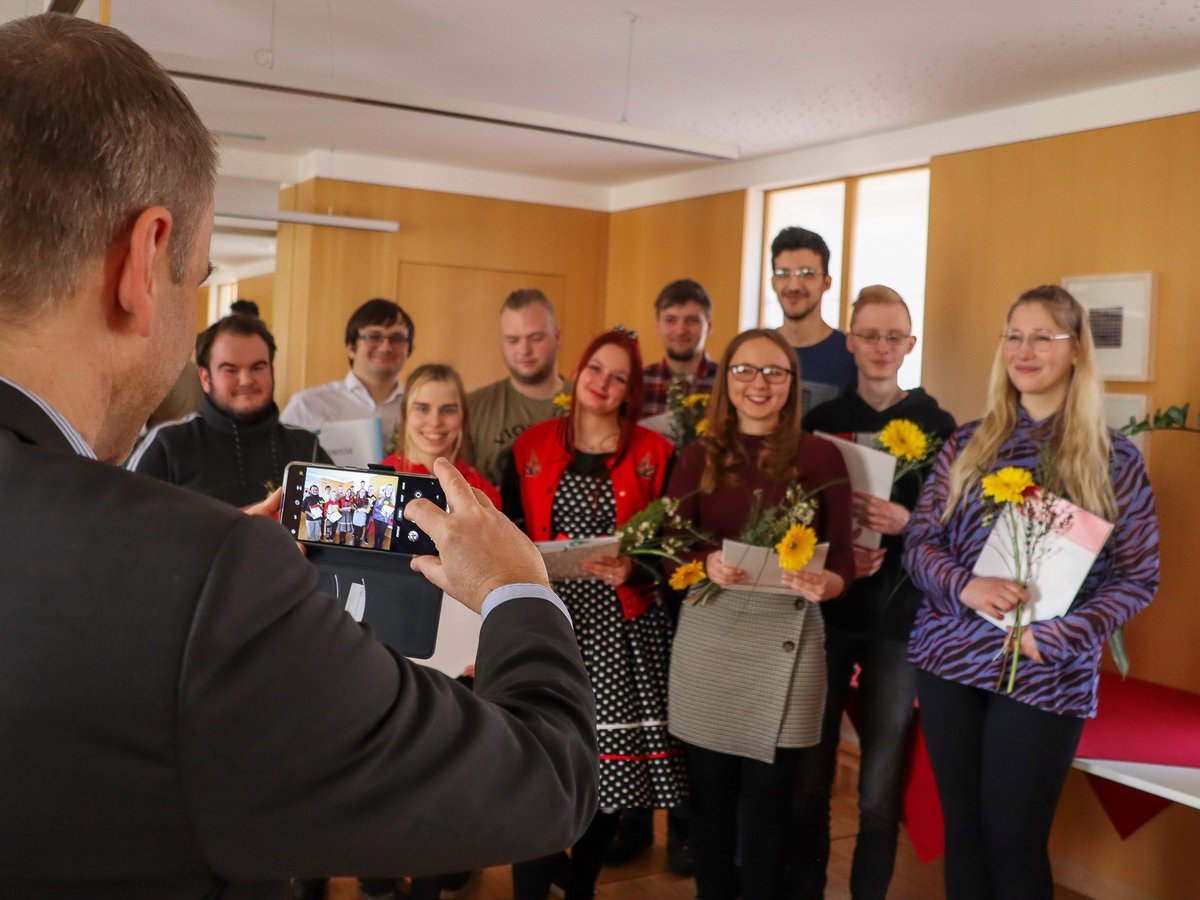Ein Mann fotografiert eine Gruppe lächelnder junger Leute, die Blumen und Zeugnisse bei einer Feier halten.