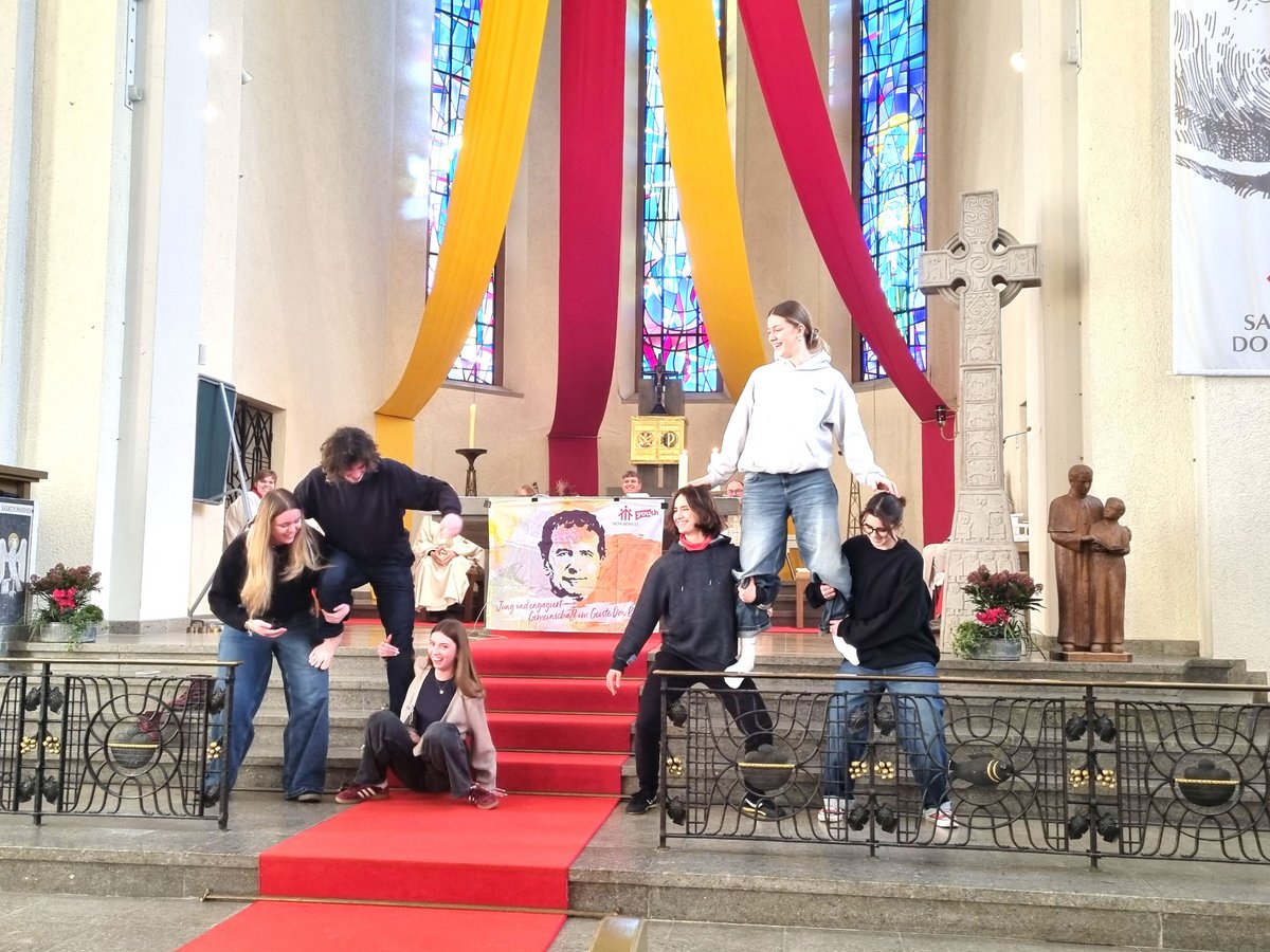 Jugendliche führen Akrobatik und Menschenpyramiden auf einem roten Teppich in einer Kirche mit Don Bosco Bannern auf.
