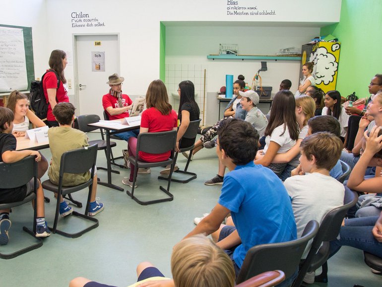 Vielfältige Gruppe von Schülern und Erwachsenen in einer interaktiven Diskussion in einem modernen Klassenzimmer.