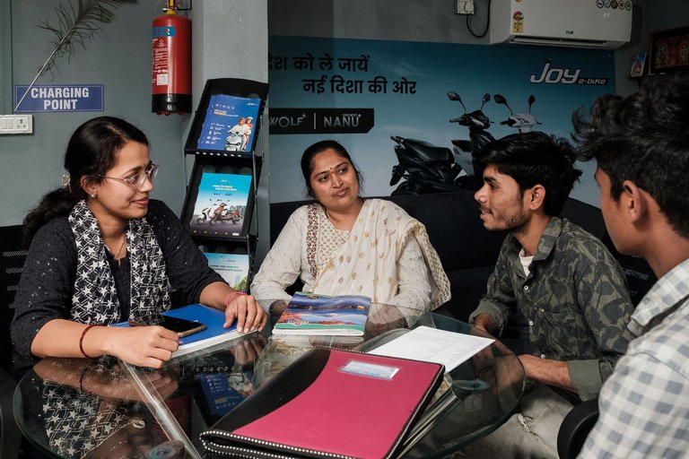 Zwei Frauen und zwei Männer sitzen an einem Glastisch in einem Büro oder Showroom und unterhalten sich.