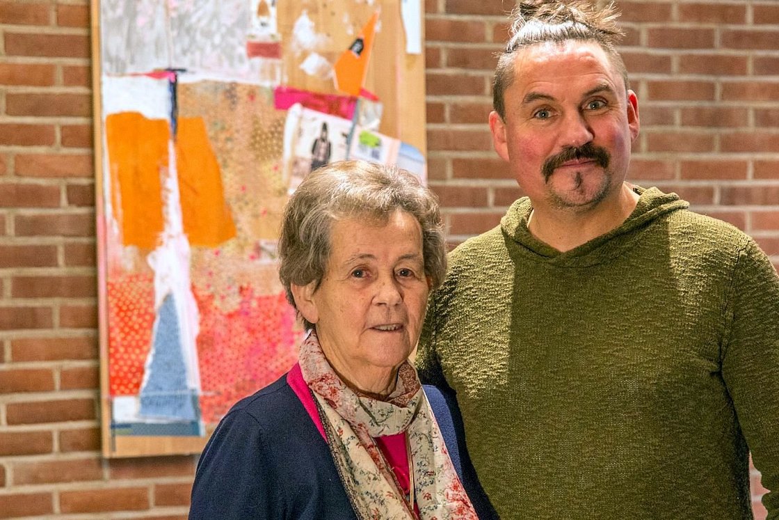 Zwei Menschen stehen vor einer Steinmauer und lächeln.