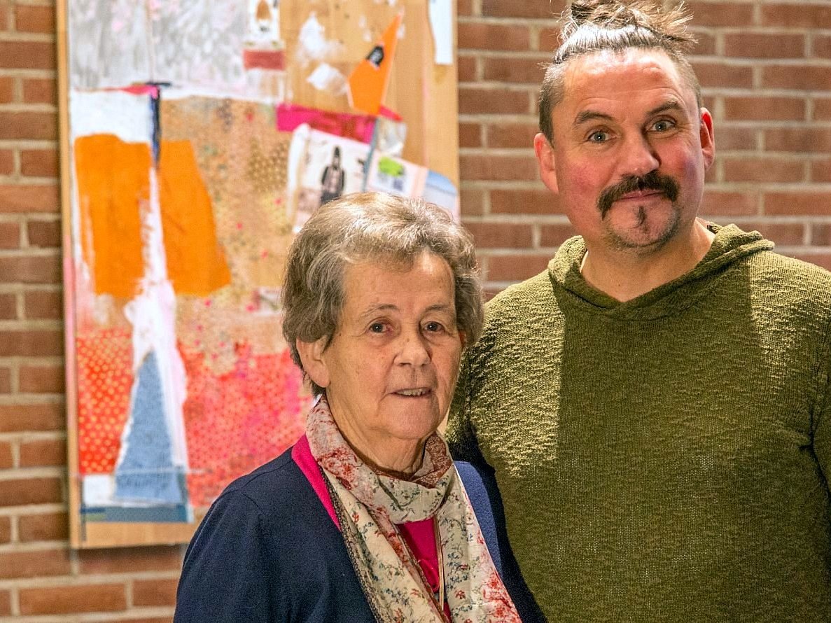 Zwei Menschen stehen vor einer Steinmauer und lächeln.