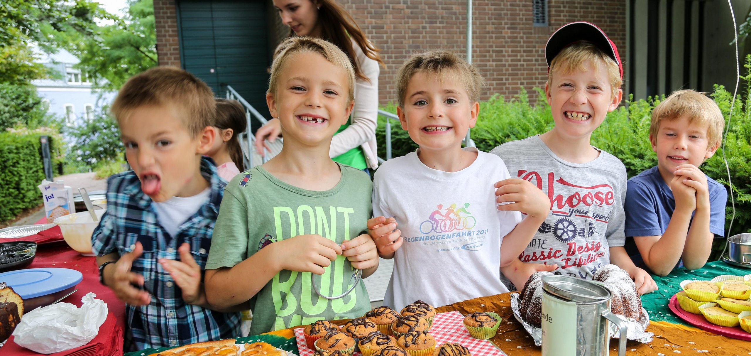 Fünf Jungen verkaufen fröhlich Kuchen und Muffins an einem Stand für eine Spendenaktion für Straßenkinder.