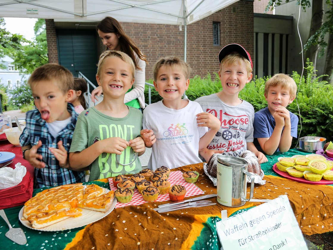 Fünf Jungen verkaufen fröhlich Kuchen und Muffins an einem Stand für eine Spendenaktion für Straßenkinder.