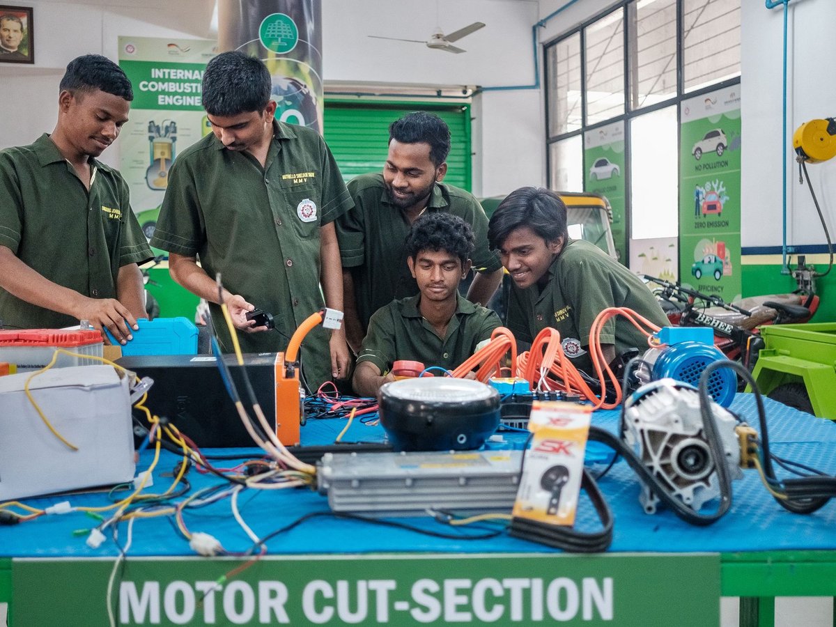 Sechs junge Männer in grünen Uniformen arbeiten konzentriert an Elektromotorkomponenten in einem Schulungsraum.