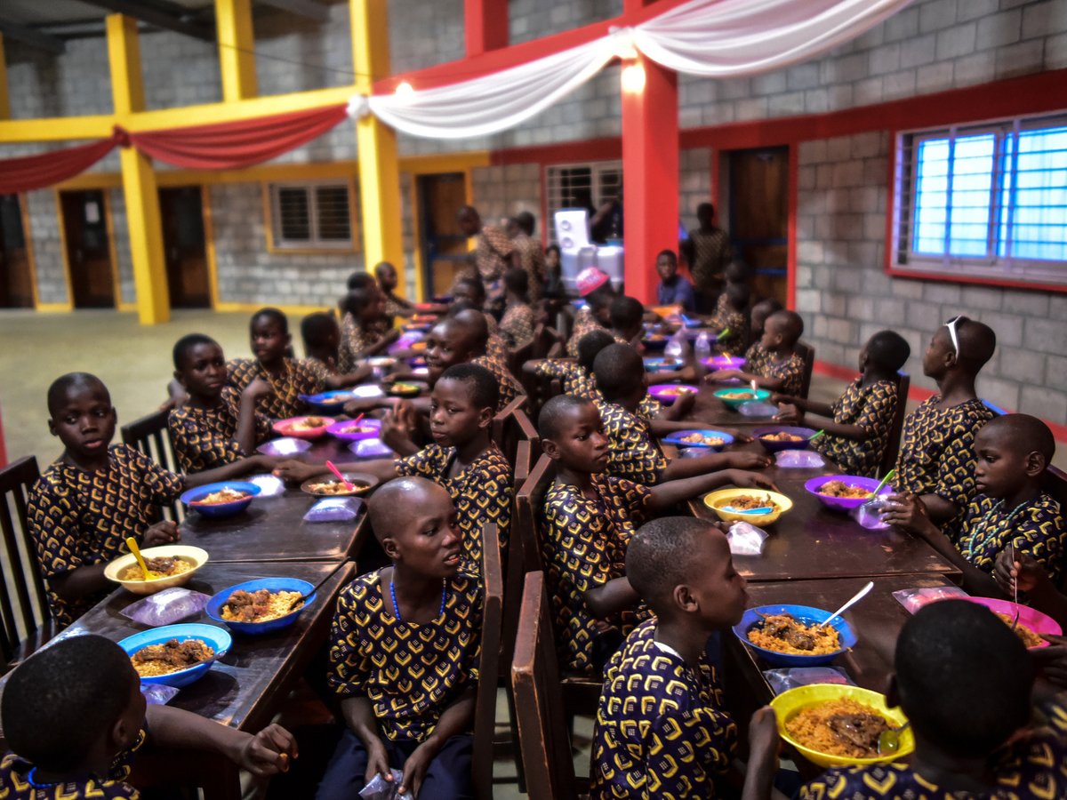Kinder in passenden gemusterten Hemden essen Mahlzeiten aus bunten Schüsseln an langen Tischen in einem dekorierten Saal.