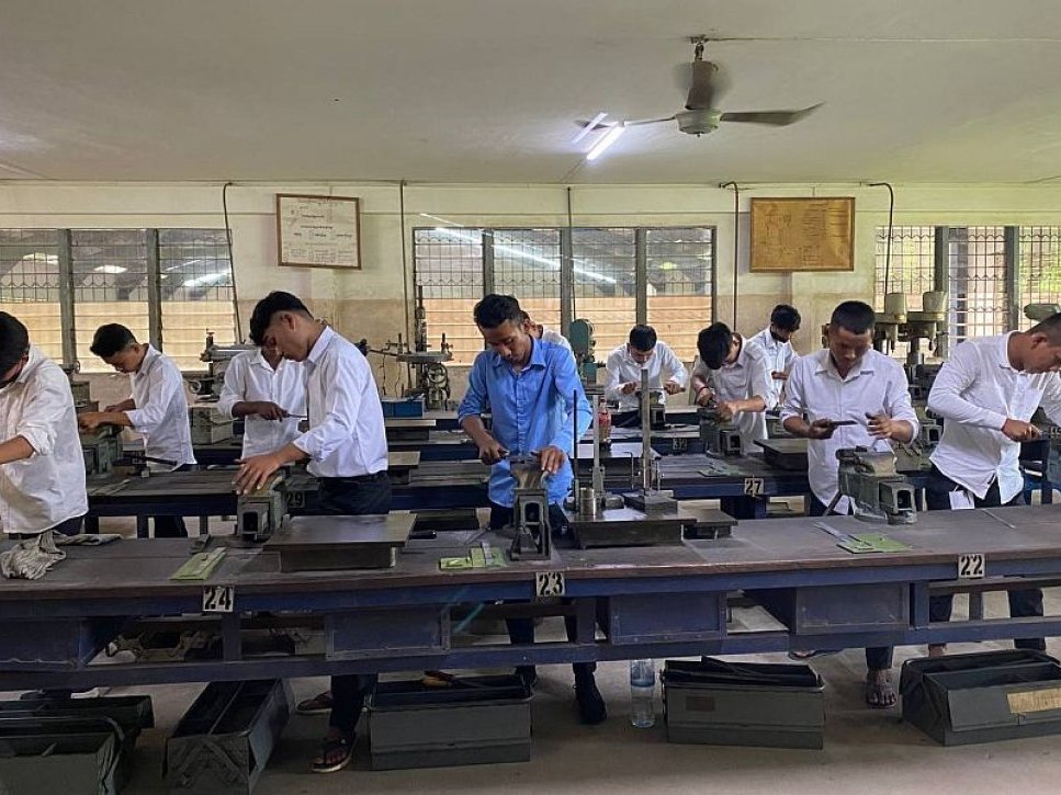 Junge Männer trainieren in einer Berufswerkstatt, nutzen Handwerkzeuge an einzelnen Bänken für praktische Fertigkeiten.