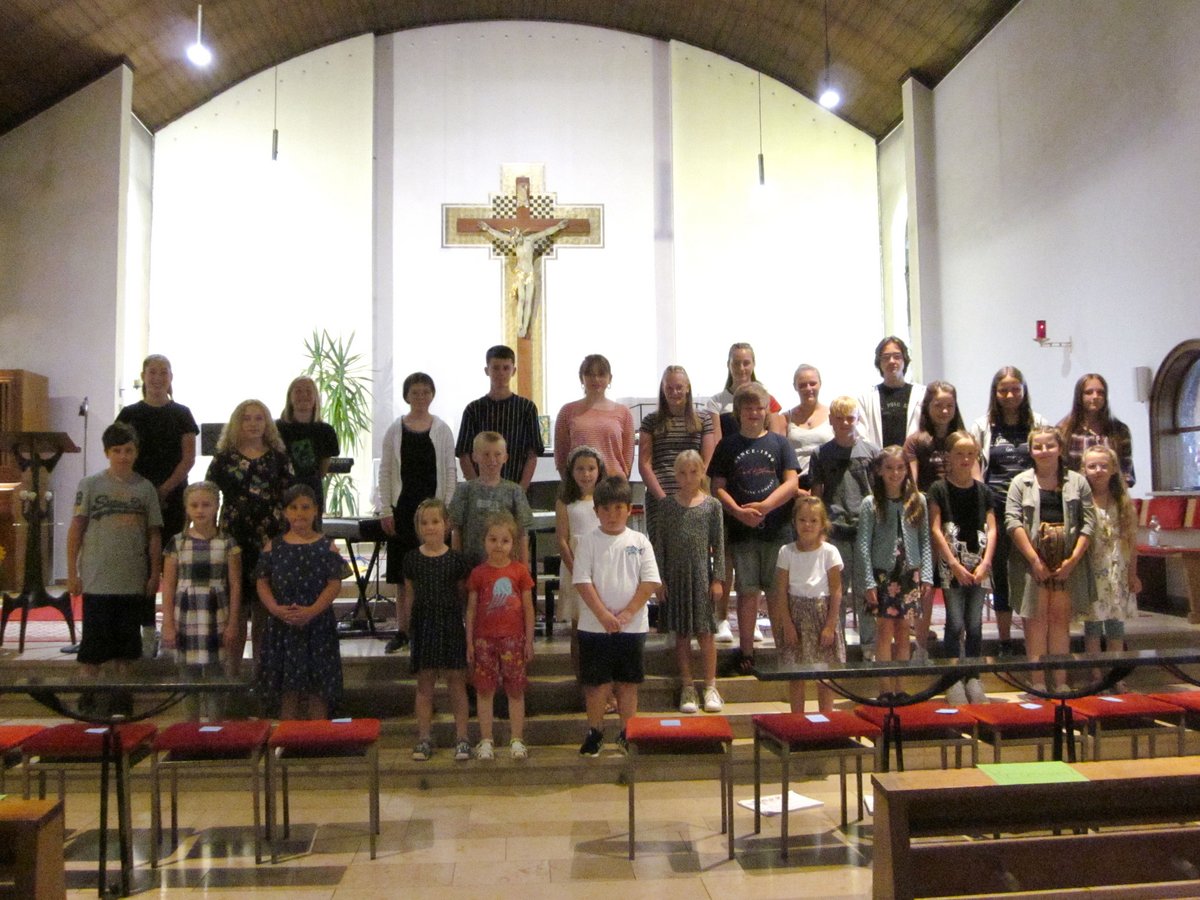 Eine Gruppe Kinder und Jugendlicher steht in Reihen in einer Kirche vor einem Altar mit einem großen Kruzifix.
