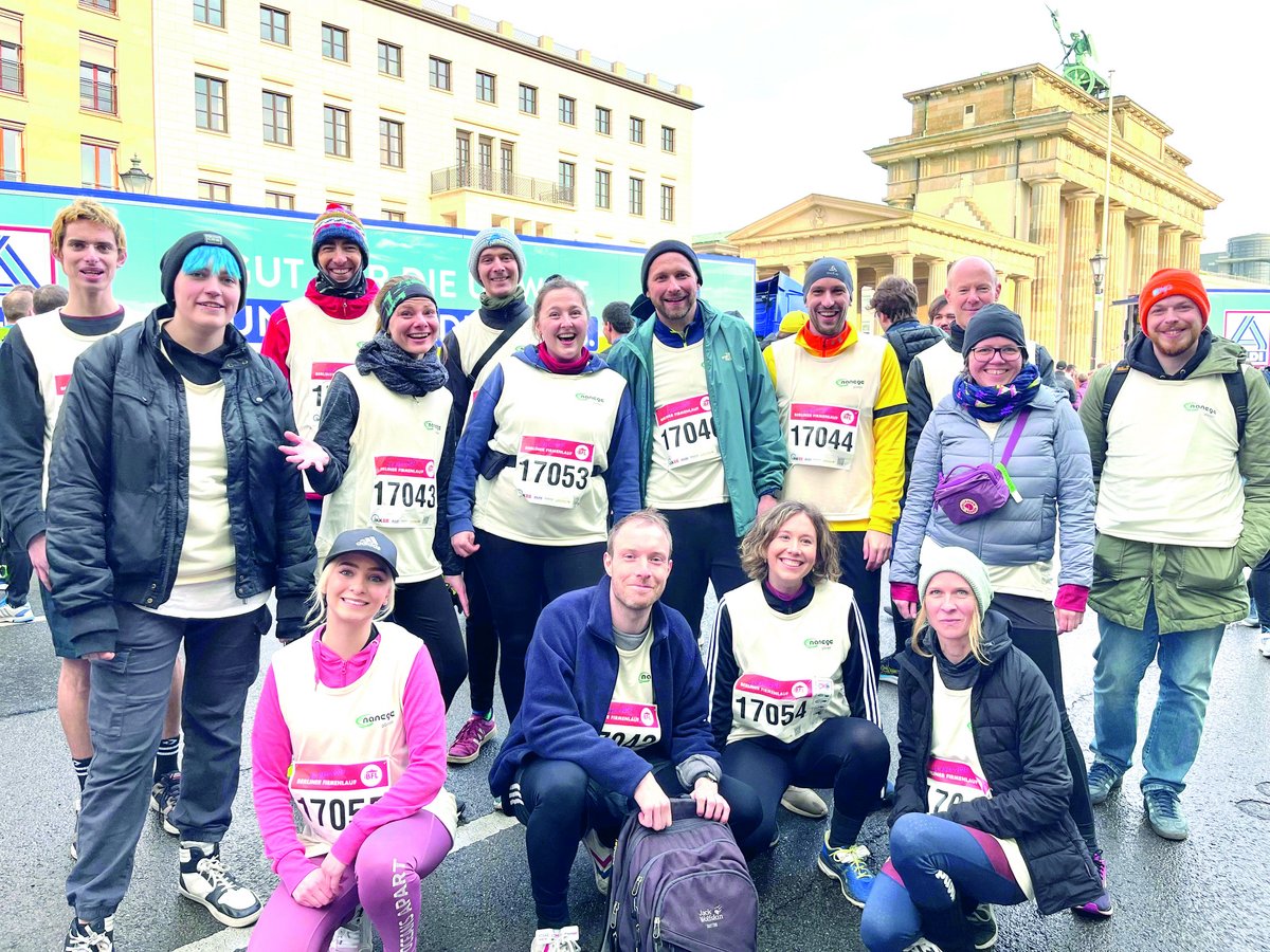 Läufergruppe des Berliner Firmenlaufs 2024 posiert lächelnd vor dem Brandenburger Tor.