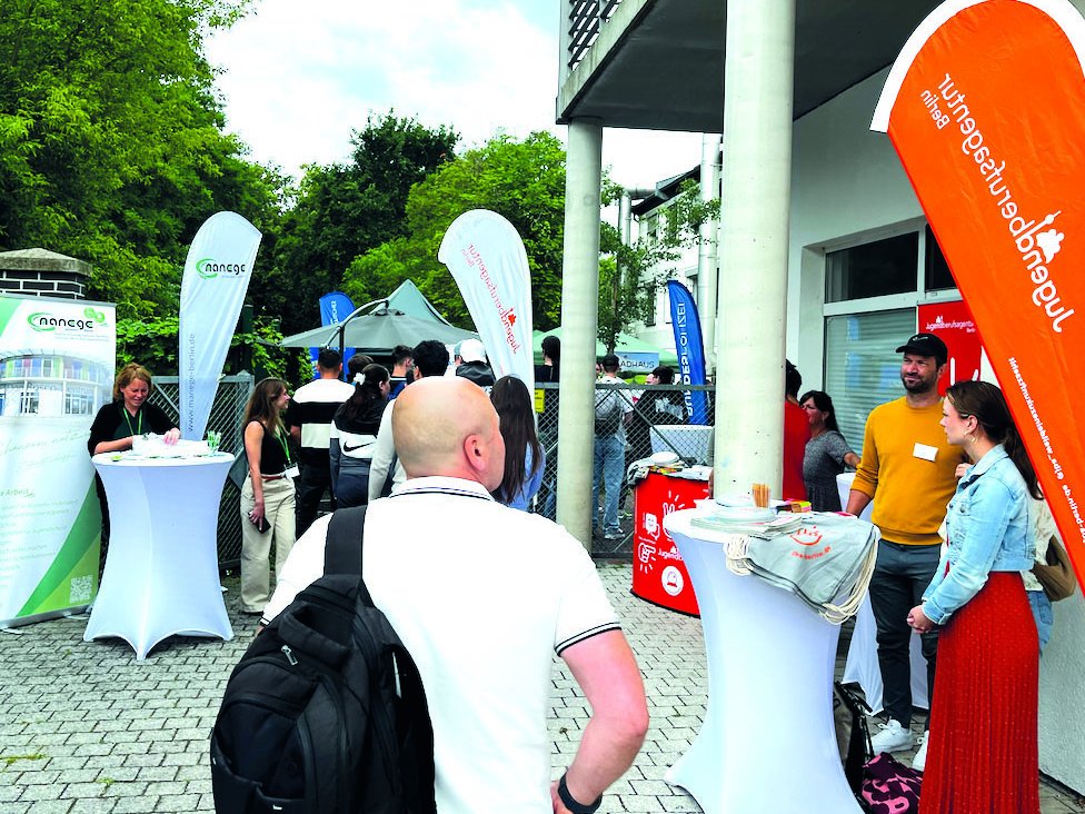 Outdoor-Veranstaltung mit Infoständen, Besuchern und großen Fahnen der Jugendberufsagentur und manaege Berlin.