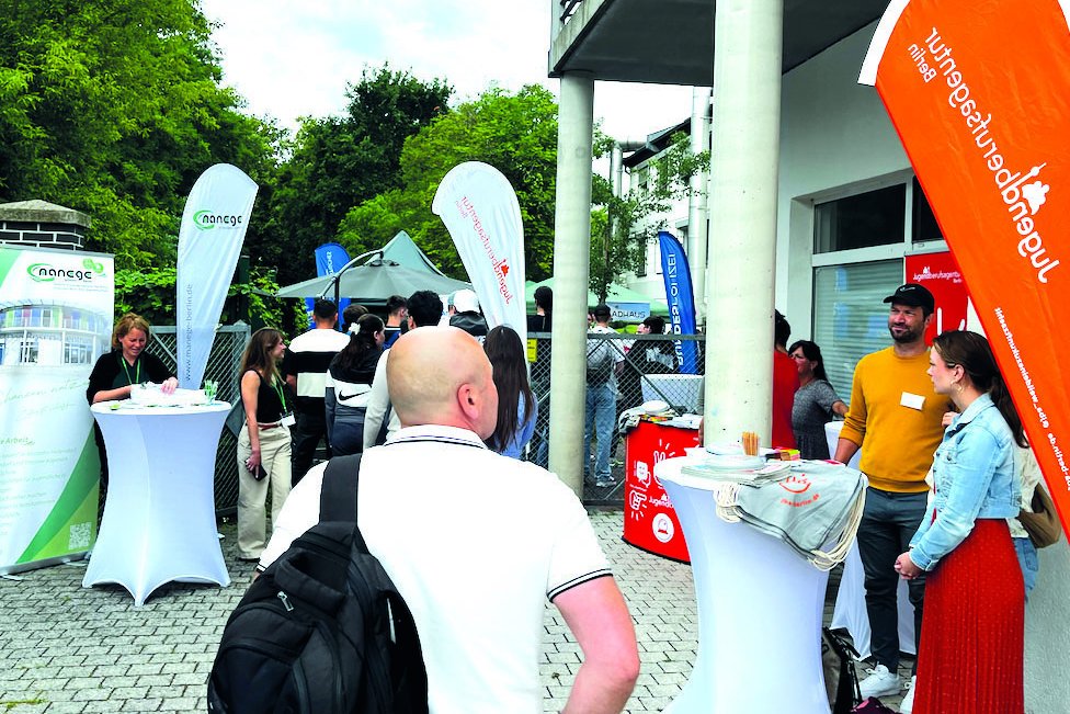 Outdoor-Veranstaltung mit Infoständen, Besuchern und großen Fahnen der Jugendberufsagentur und manaege Berlin.