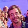 Chekcer Tobi sieht in eine Handykamera, daneben sitzen Kinder