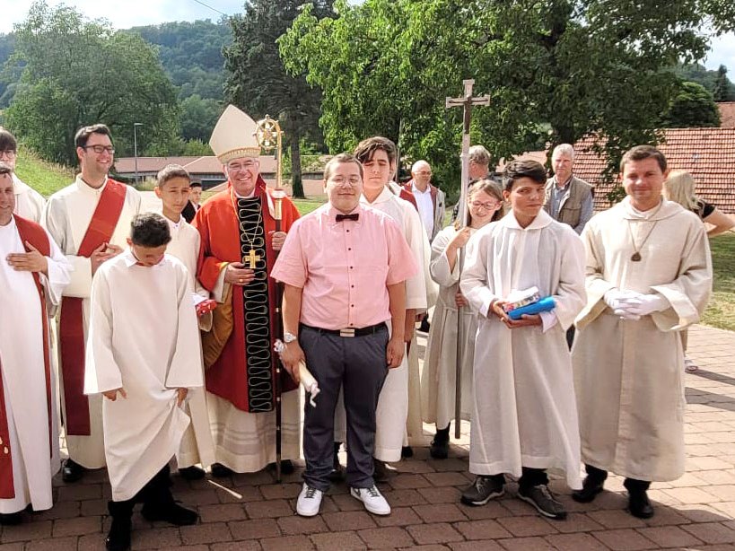 Bischof, Priester, Ministranten und ein junger Mann stehen nach einer religiösen Zeremonie festlich im Freien.