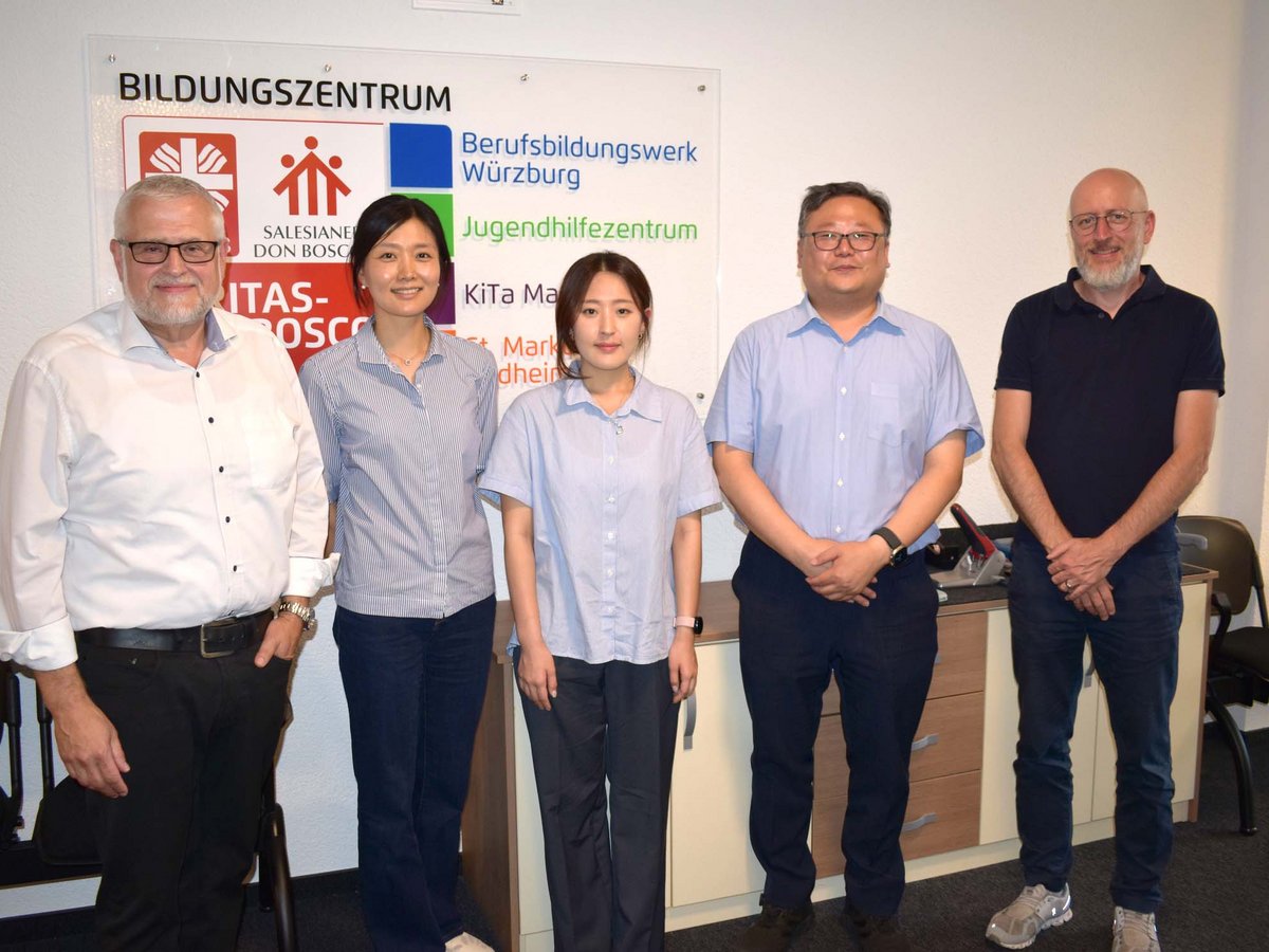 Fünf Personen, drei Männer und zwei Frauen, stehen vor einem Schild eines deutschen Bildungszentrums.