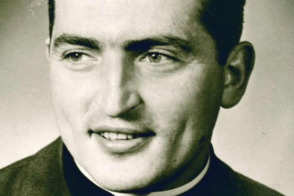 Porträt eines lächelnden jungen Priesters mit dunklem Haar und Kollar, leicht zur Seite blickend, Vintage-Foto.