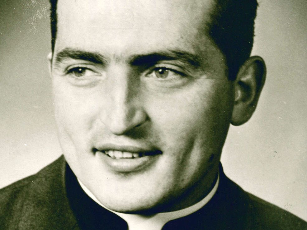 Porträt eines lächelnden jungen Priesters mit dunklem Haar und Kollar, leicht zur Seite blickend, Vintage-Foto.