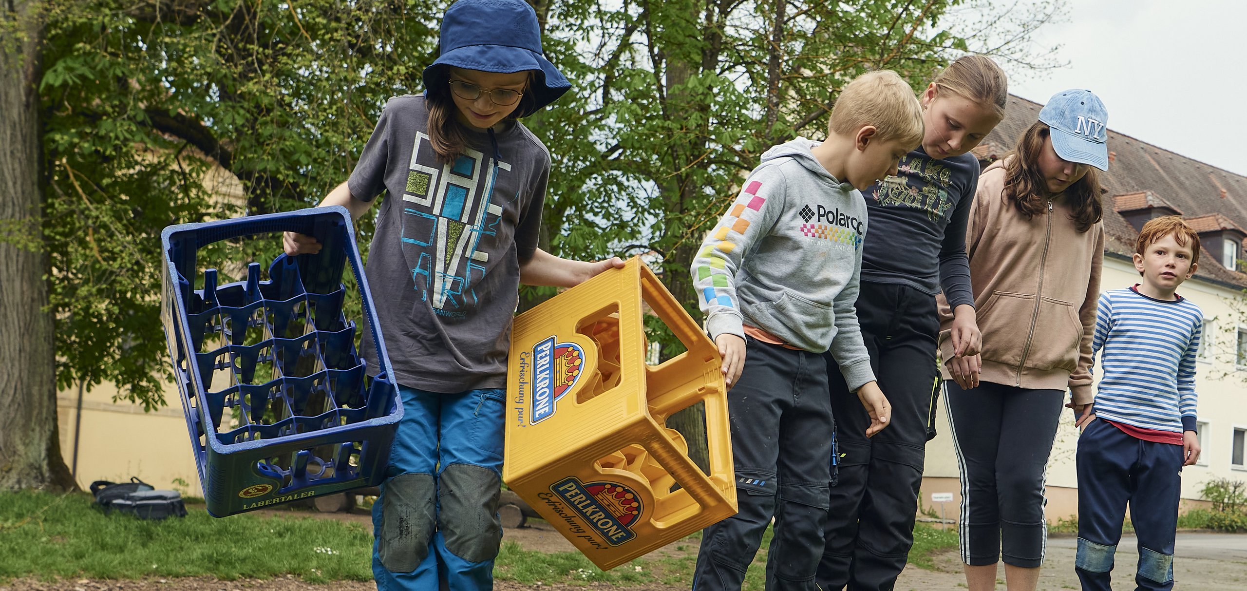 Kinder auf der Wiese auf Bierkisten stehend vor Gebäude