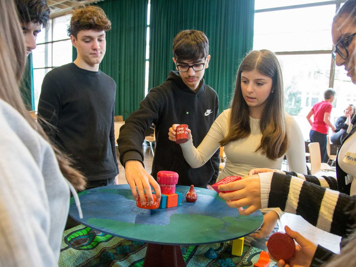 Jugendliche platzieren farbige Objekte auf einem Weltkugel-Tisch bei einem Workshop zum Thema globale Zusammenhänge.