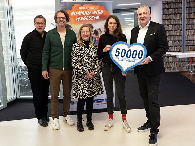 Fünf Personen halten stolz ein herzförmiges Schild '50000 Sparda-Bank', wahrscheinlich eine Spende für 'Niemand wird vergessen'.