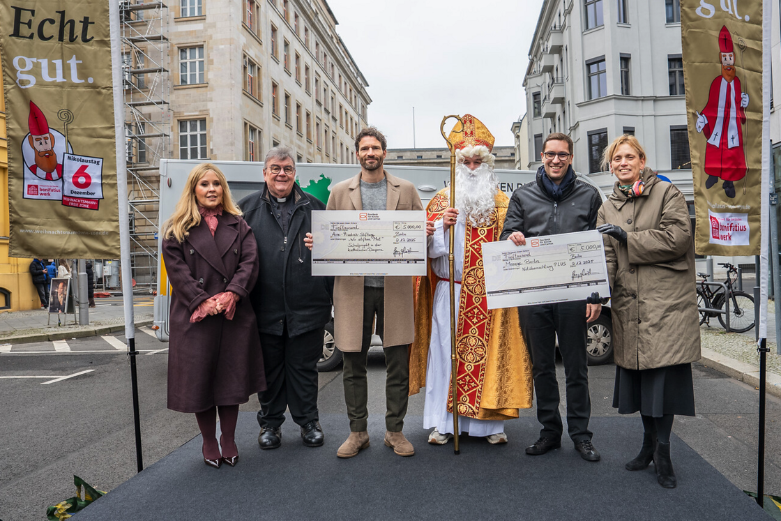 Sechs Personen, darunter ein Priester und der Nikolaus, präsentieren Spendenschecks einer Bonifatiuswerk-Kampagne.