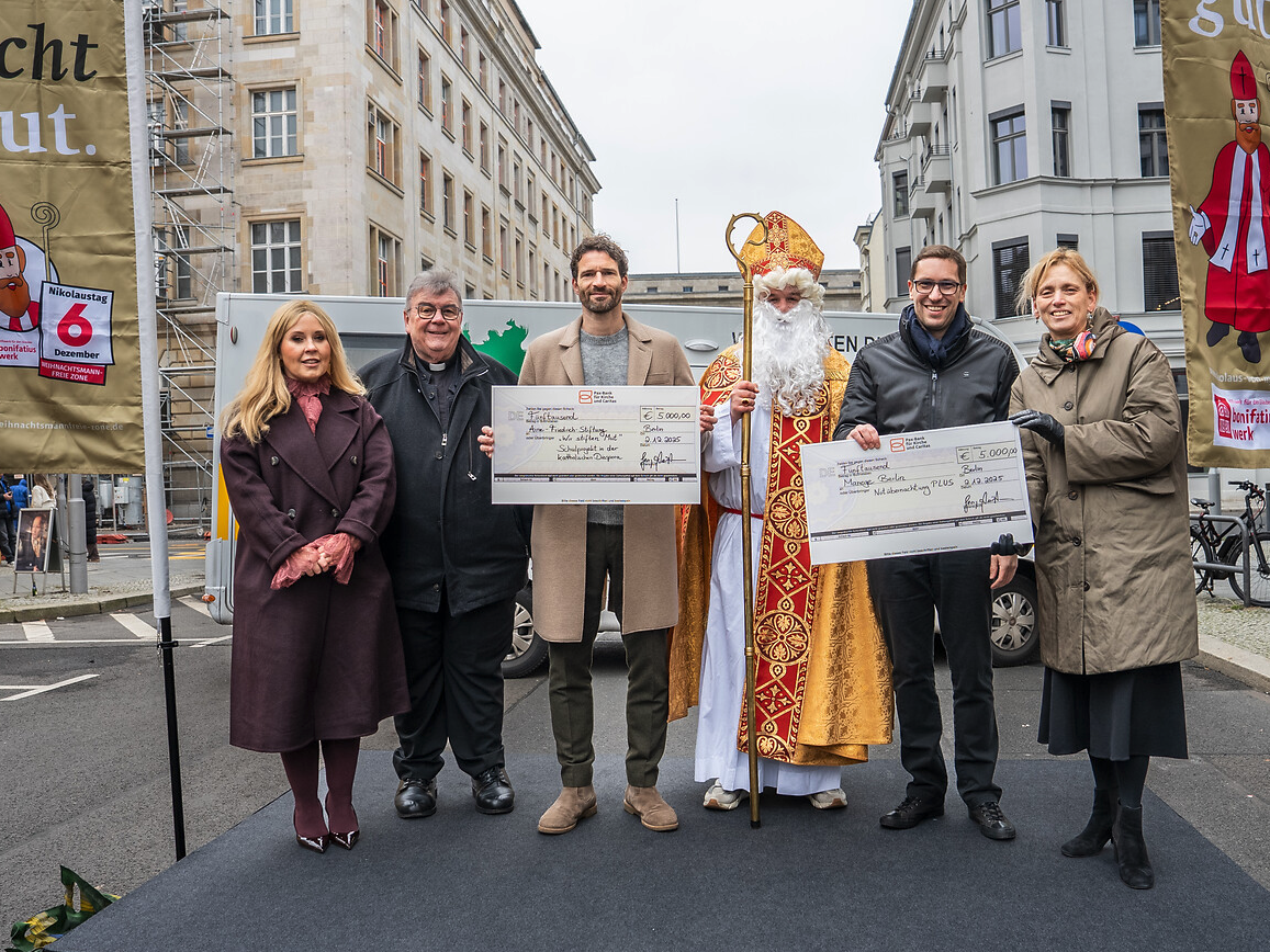 Sechs Personen, darunter ein Priester und der Nikolaus, präsentieren Spendenschecks einer Bonifatiuswerk-Kampagne.