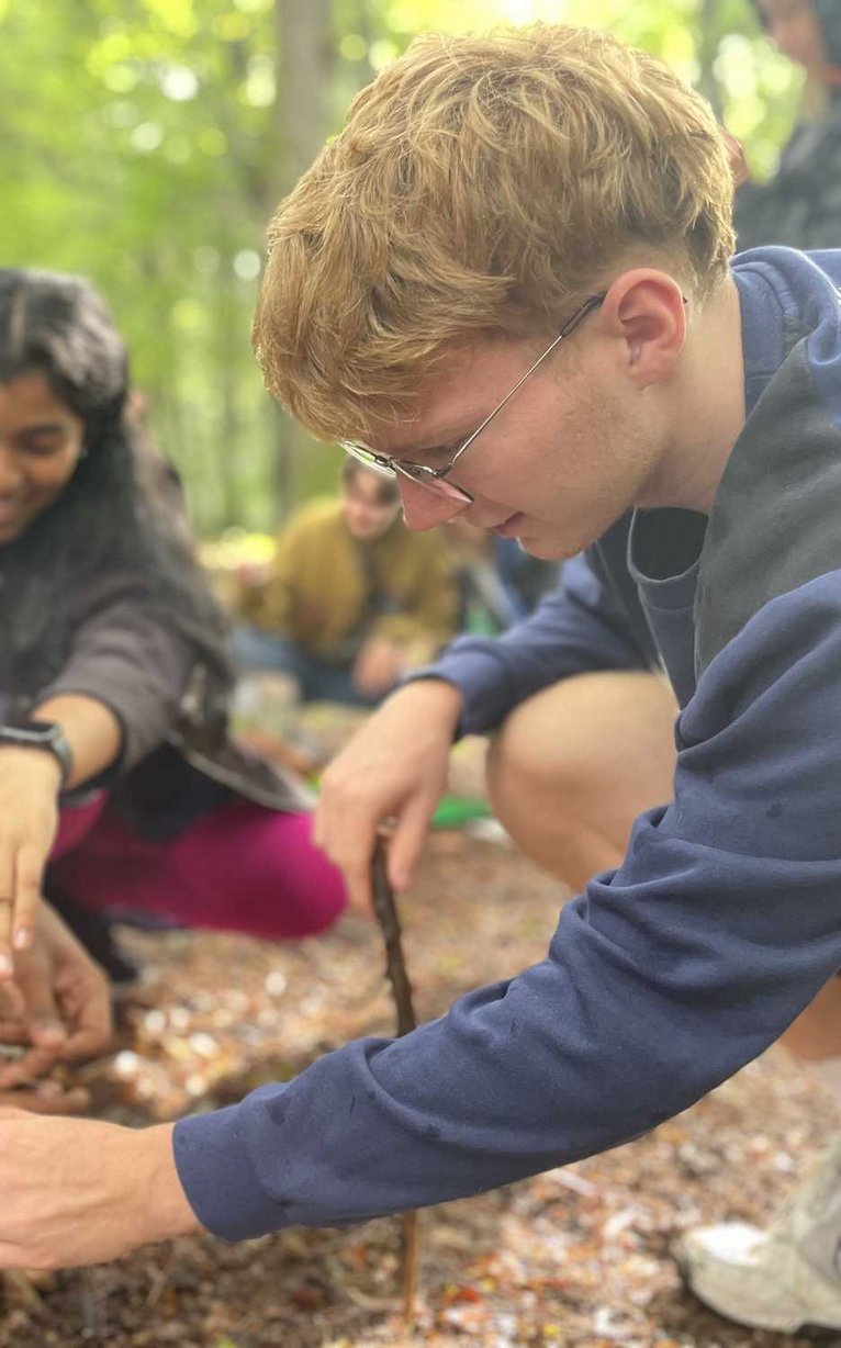 Drei junge Leute hocken im Wald und pflanzen gemeinsam einen kleinen Baum oder Setzling.