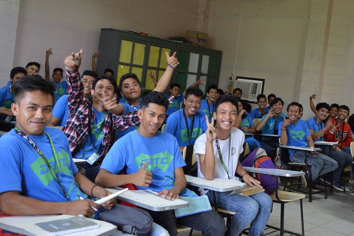 Gruppe lächelnder junger Männer in blauen T-Shirts mit verschiedenen Handgesten im Klassenzimmer.