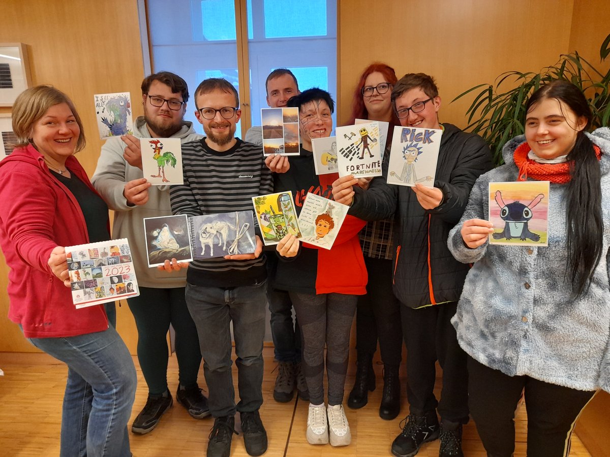 Eine Gruppe von zehn lächelnden Personen hält stolz ihre vielfältigen Kunstwerke und einen 2023-Kalender hoch.