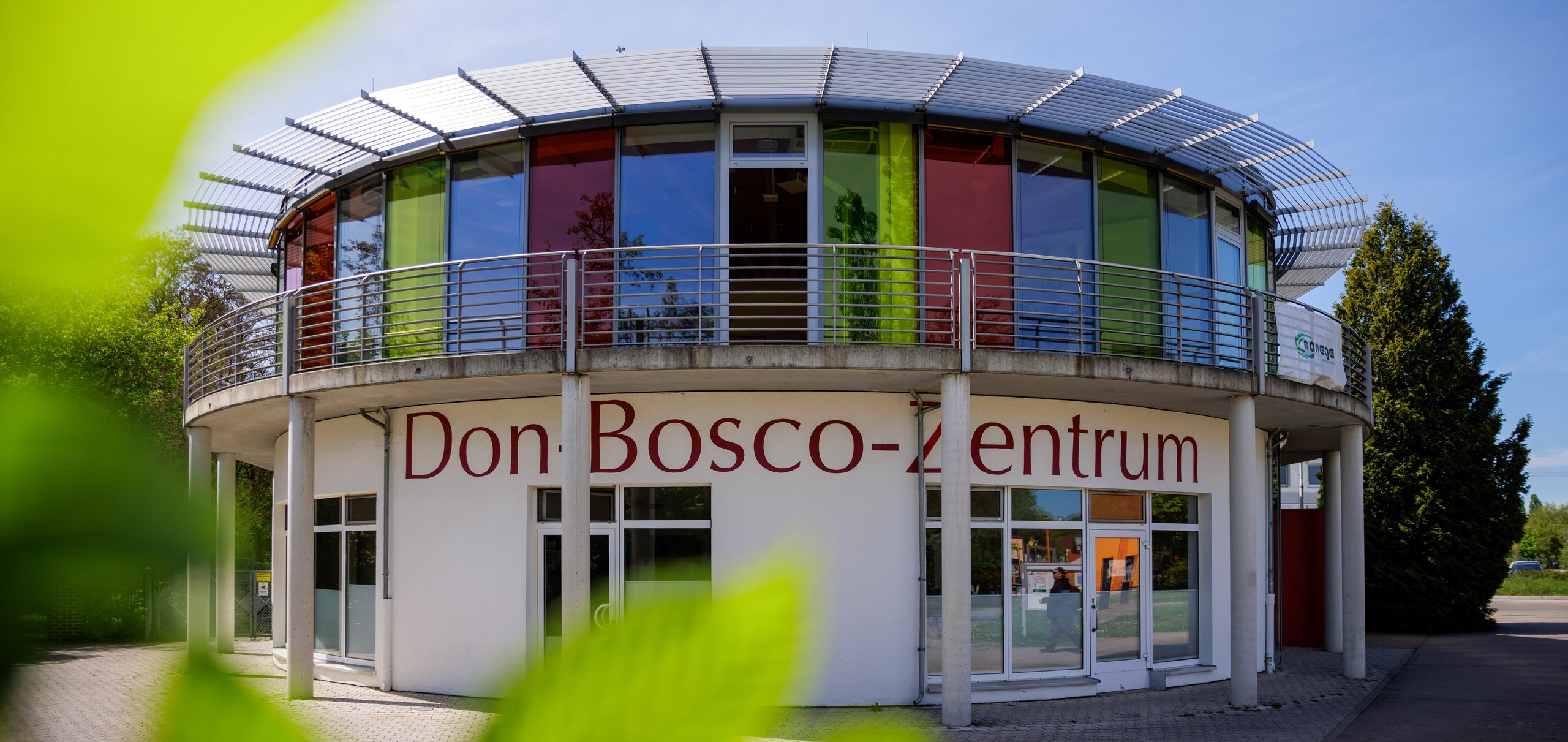 Rundes Gebäude mit Blättern davor und Schrift darauf Don Bosco Zentrum