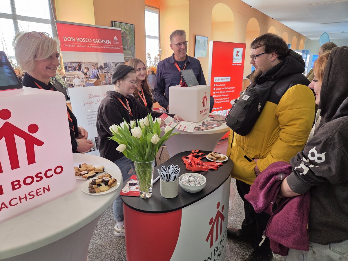 Mehrere Personen unterhalten sich an Messeständen von Don Bosco Sachsen und Kaufland, umgeben von Infomaterial und Snacks.