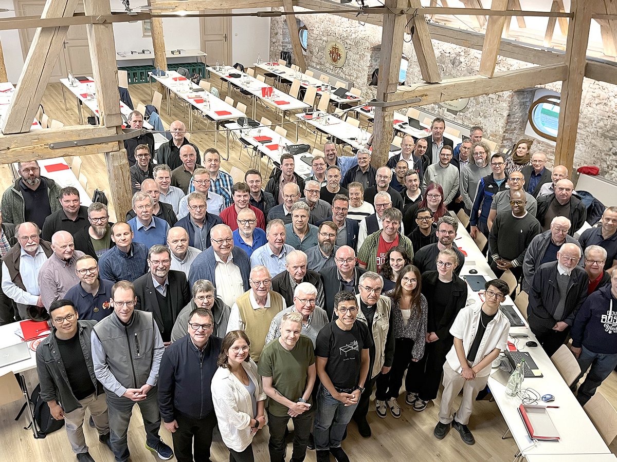 Große Gruppe von Personen, hauptsächlich Männer, die in einem rustikalen Konferenzraum mit Holzbalken für ein Foto posieren.