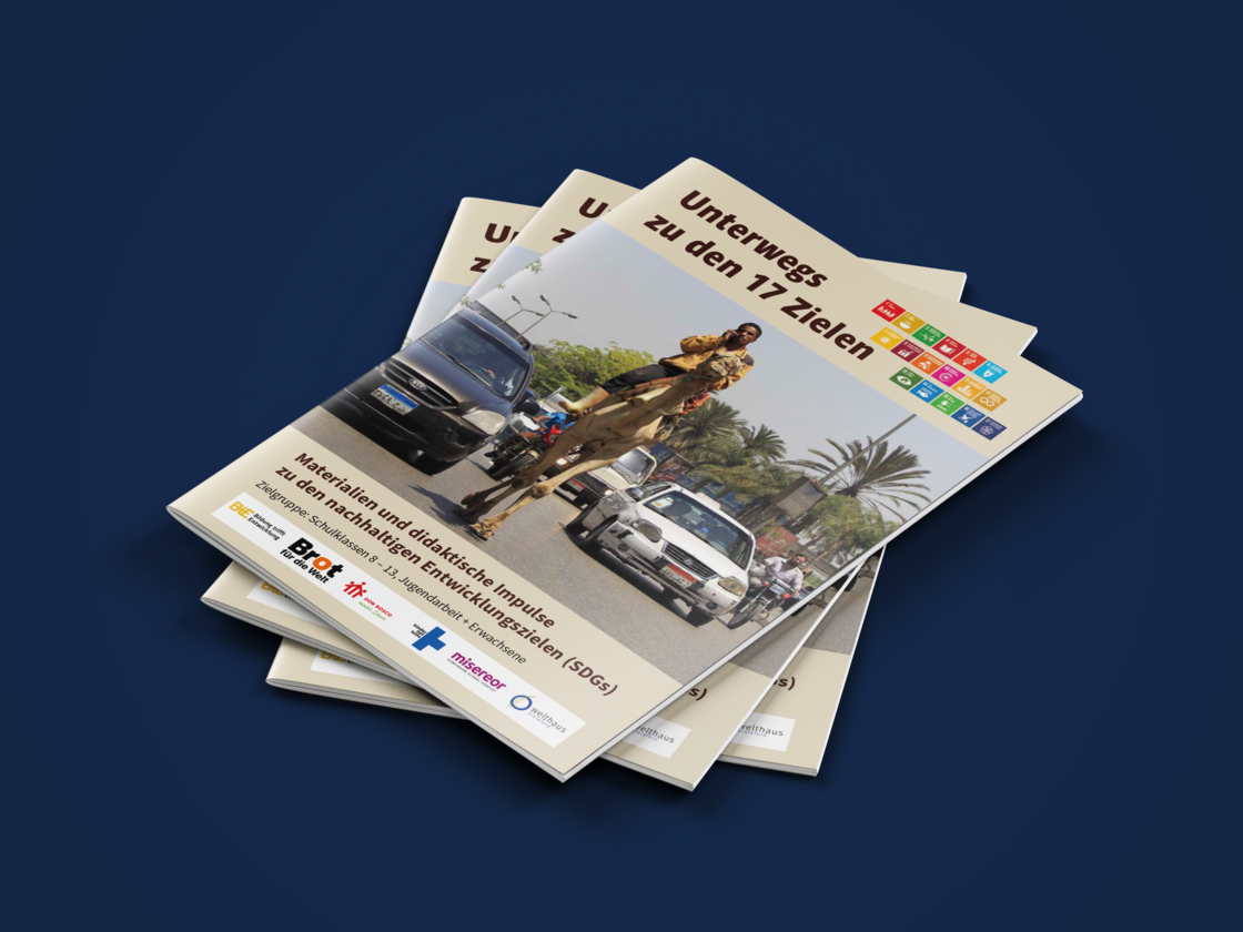 Stapel "Unterwegs zu den 17 Zielen"-Broschüren; Titelbild: Mann auf Kamel im Straßenverkehr mit Autos und Palmen.