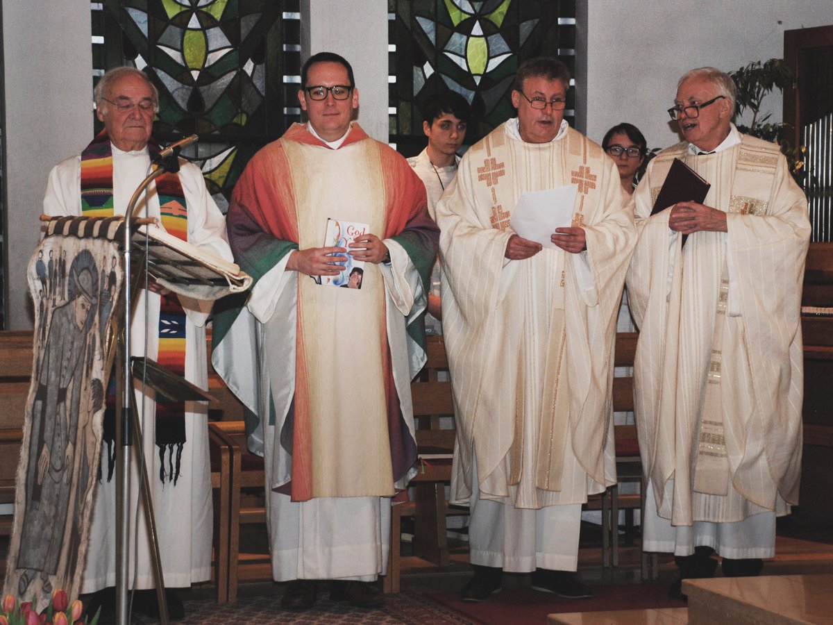 Fünf Priester und Diakone in liturgischen Gewändern stehen in einer Kirche, einige halten Bücher, bei einem Gottesdienst.