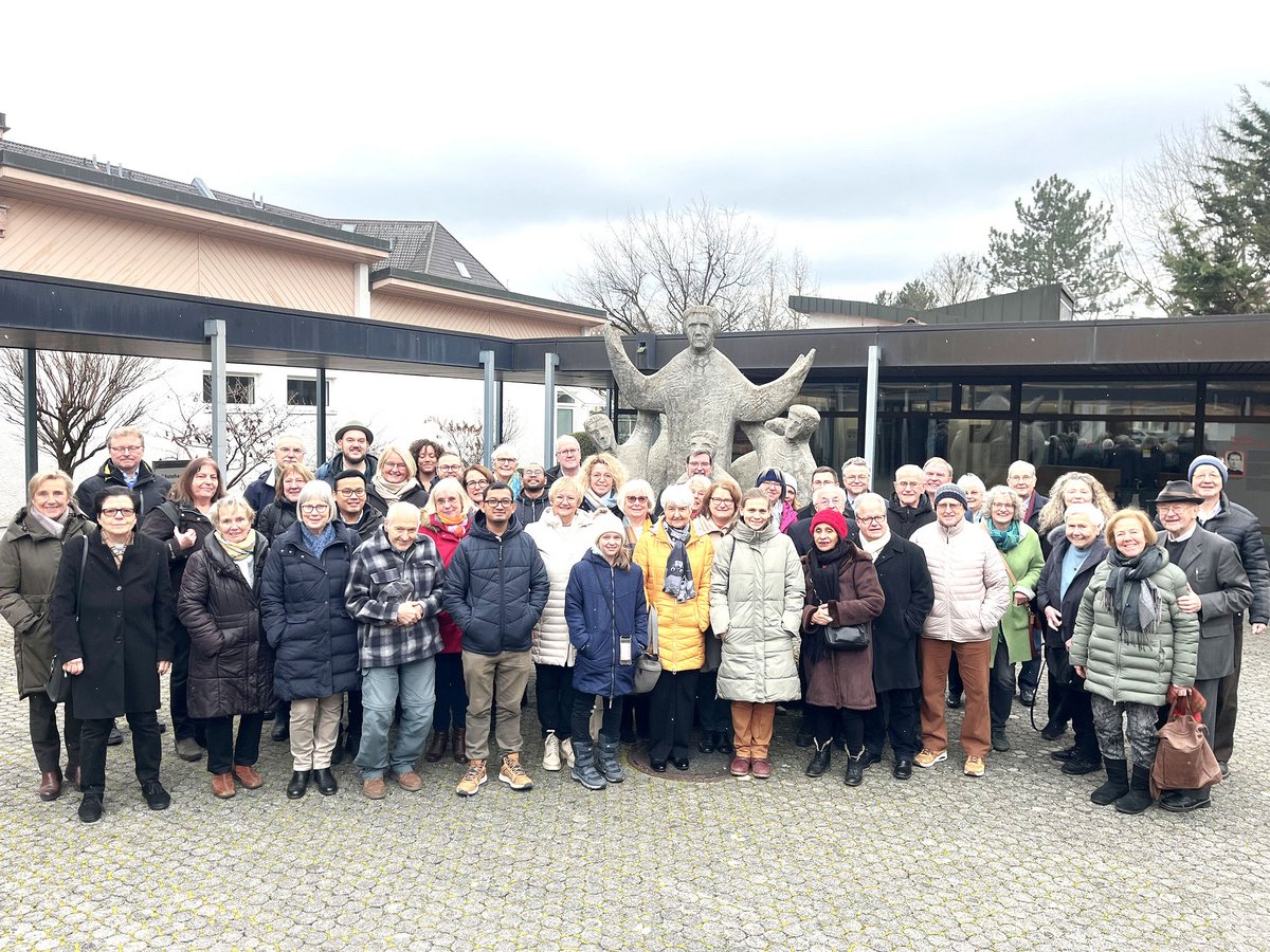 Lachende Gruppe von Menschen unterschiedlichen Alters in Winterkleidung posiert vor einem Gebäude und einer Statue.