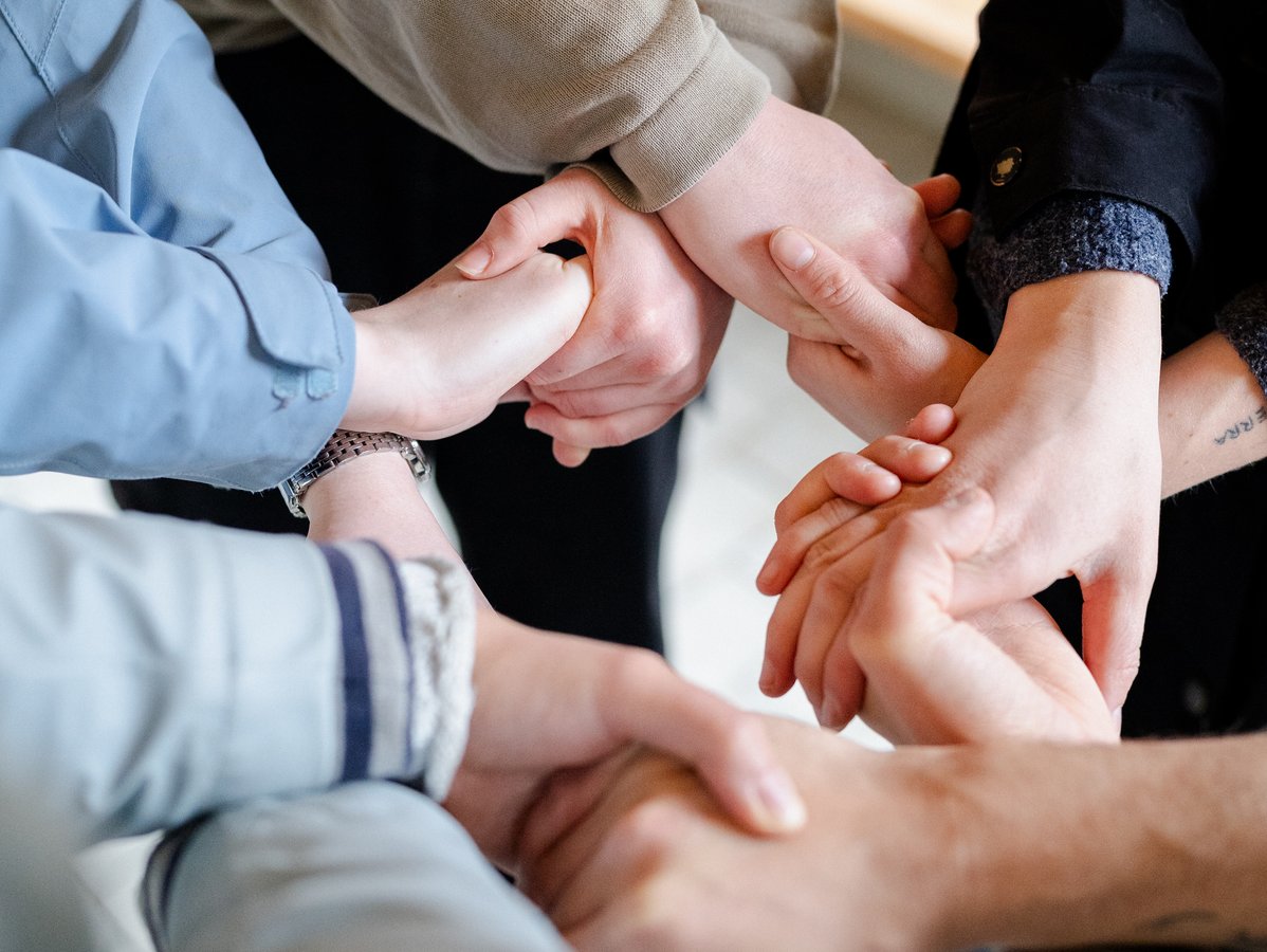 Nahaufnahme mehrerer in einem Kreis verschränkter Hände, die Einheit, Teamarbeit und Unterstützung symbolisieren.