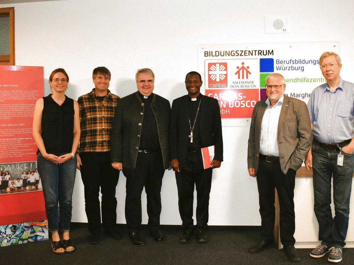 Gruppenfoto von sieben Personen, darunter Kleriker, vor einem Schild des Bildungszentrums Würzburg und einem Don Bosco Banner.