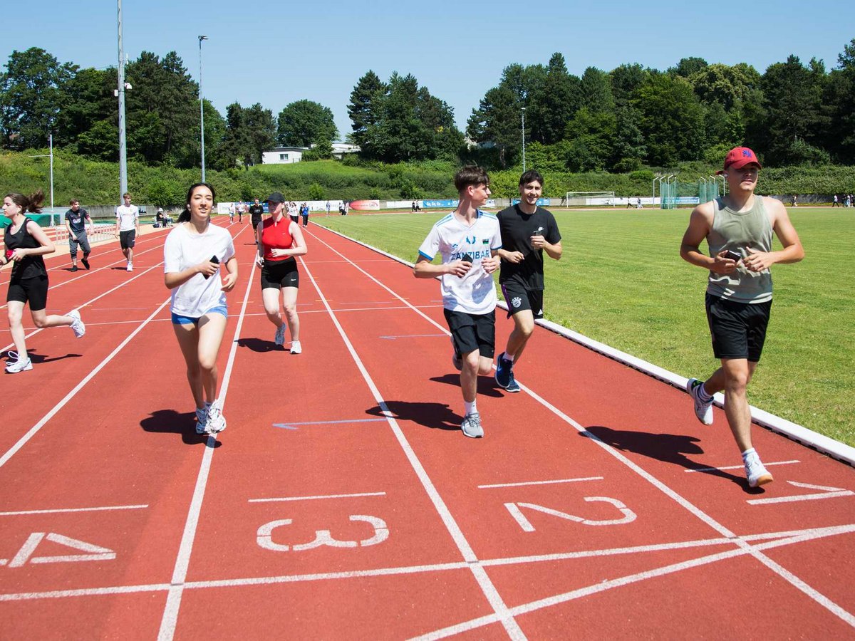 Eine Gruppe junger Leute joggt an einem sonnigen Tag auf einer roten Laufbahn im Freien.