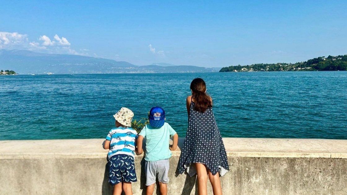 Drei Kinder lehnen an Mauer und schauen auf See